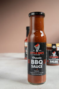 Close-up of Little Red's Award-Winning Chipotle BBQ Sauce, winner of Gold in the Condiment Category at this year's Irish Quality Food and Drink Awards. The bottle is sharply in focus with its vibrant label, while the other two sauces blur in the background, emphasizing the Chipotle BBQ Sauce's acclaimed status and rich, smoky flavor profile.
