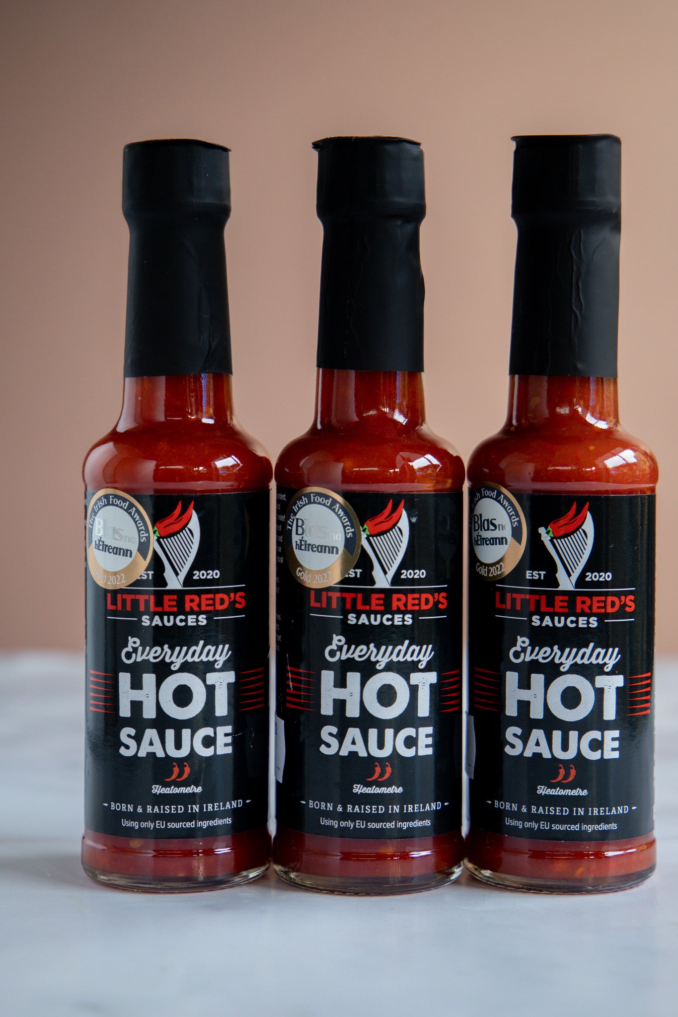 Three bottles of Little Red's Fermented Chili and Garlic Hot Sauce lined up in a row, featuring bold labels that highlight the unique fermentation process. The deep red sauce, enriched with garlic, is visible through the clear glass, presenting a tantalizing option for spice lovers and gourmet enthusiasts.