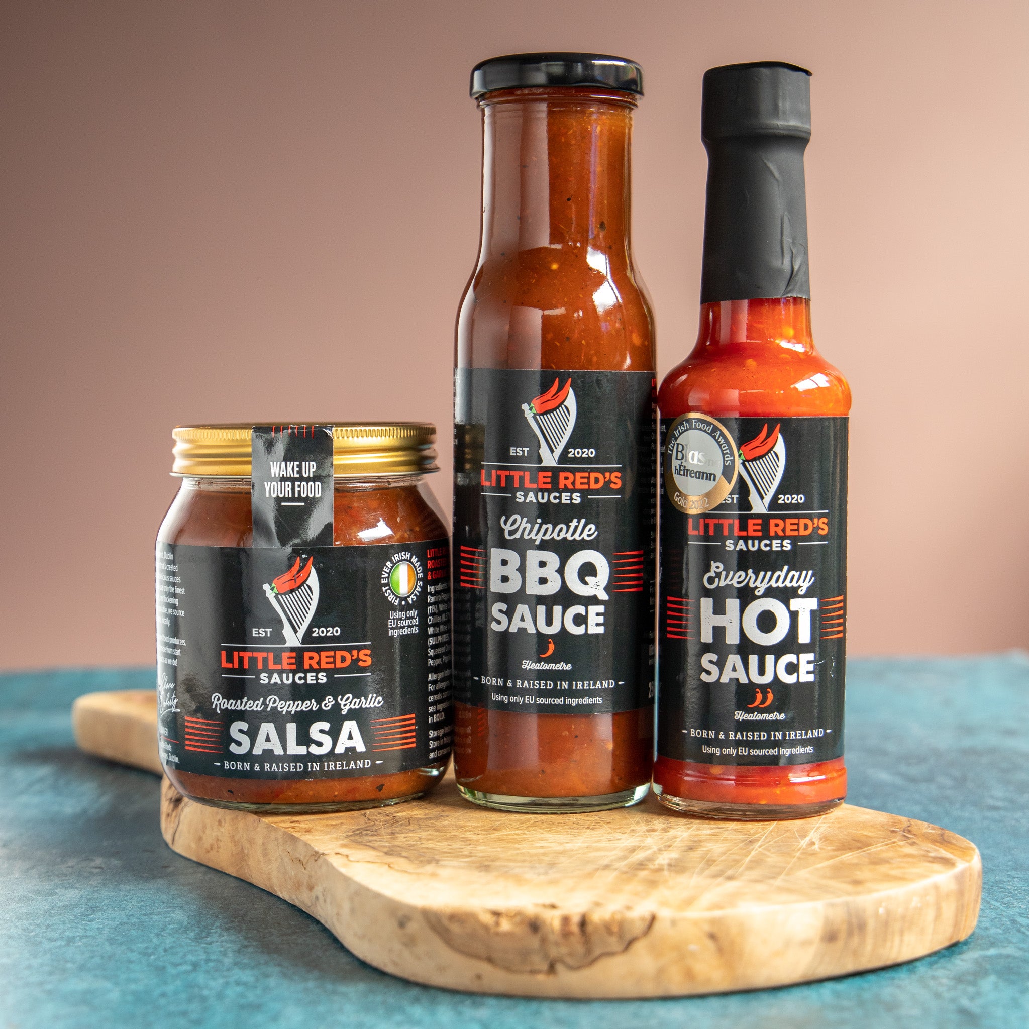 Little Red's Selection Box featuring three signature sauces displayed on a wooden chopping board. The image showcases the variety and distinct packaging of each sauce, highlighting their unique colors and labels, making an inviting visual for food enthusiasts and gift seekers.